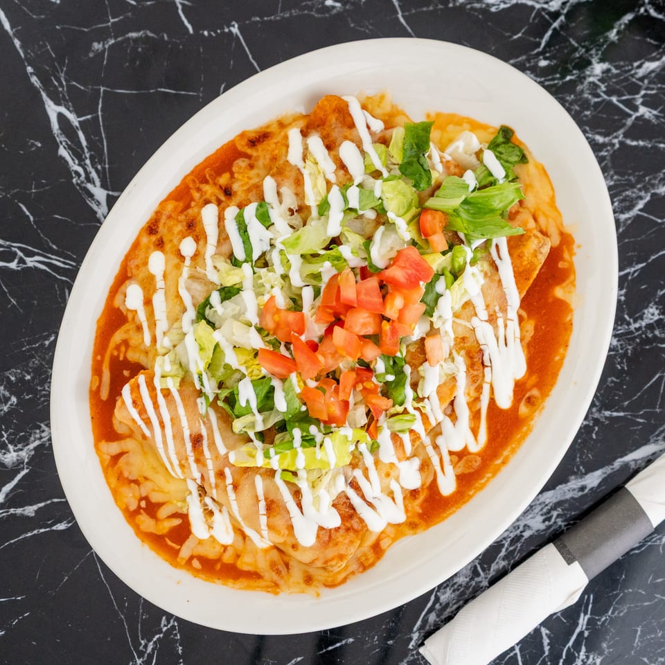 A plate of enchiladas topped with red sauce, melted cheese, lettuce, diced tomatoes, and sour cream.