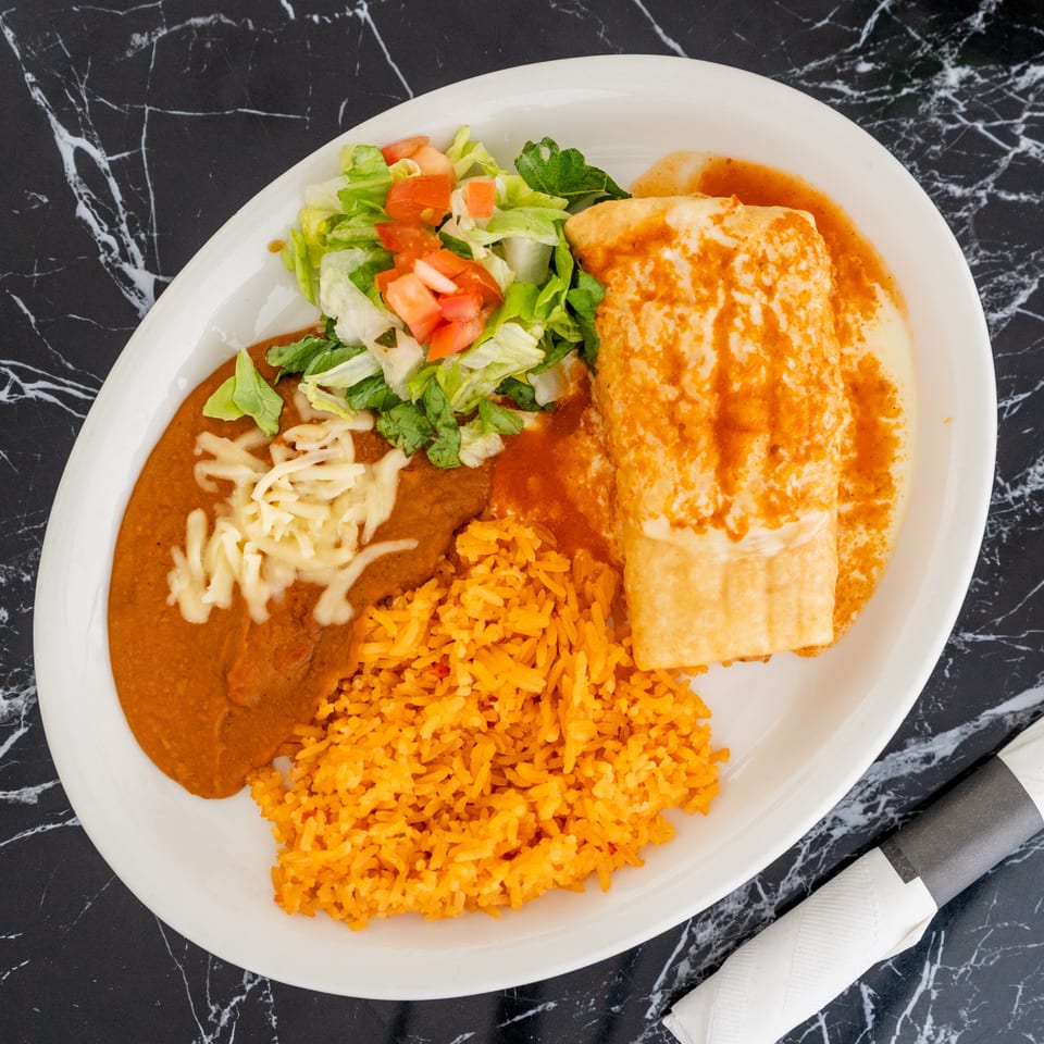 A Mexican combination plate with a burrito, refried beans, rice, and a side salad.