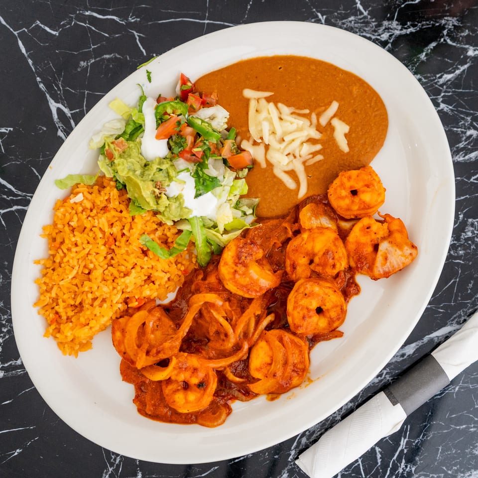 A white plate with shrimp in red sauce, rice, refried beans, and a side salad.