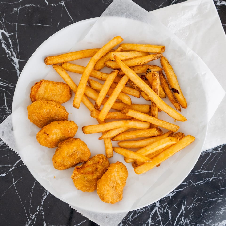 A white plate with golden chicken nuggets and crispy french fries on a black marble table.