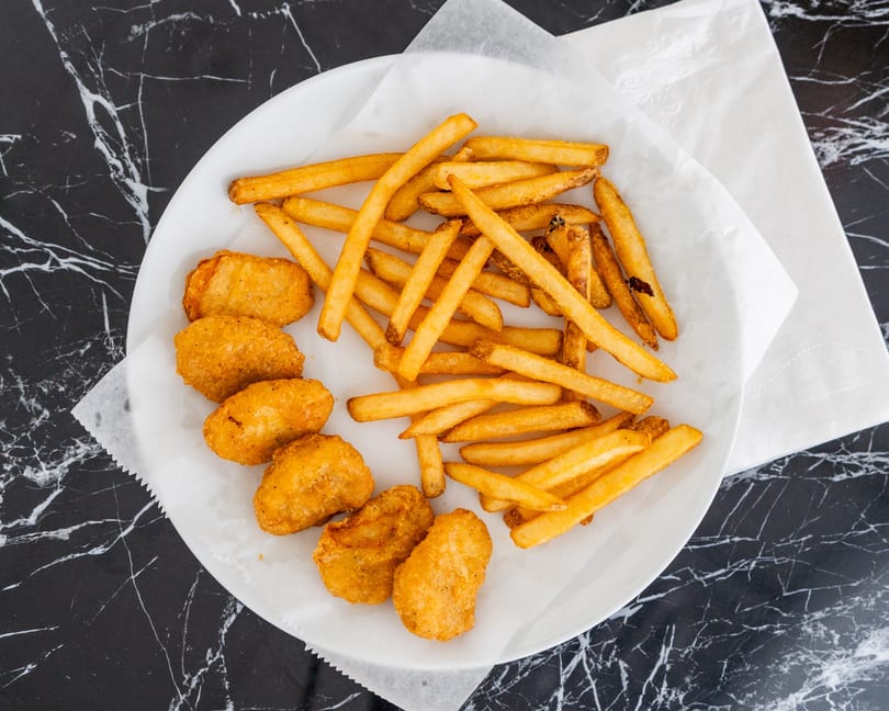 A white plate with golden chicken nuggets and crispy french fries on a black marble table.