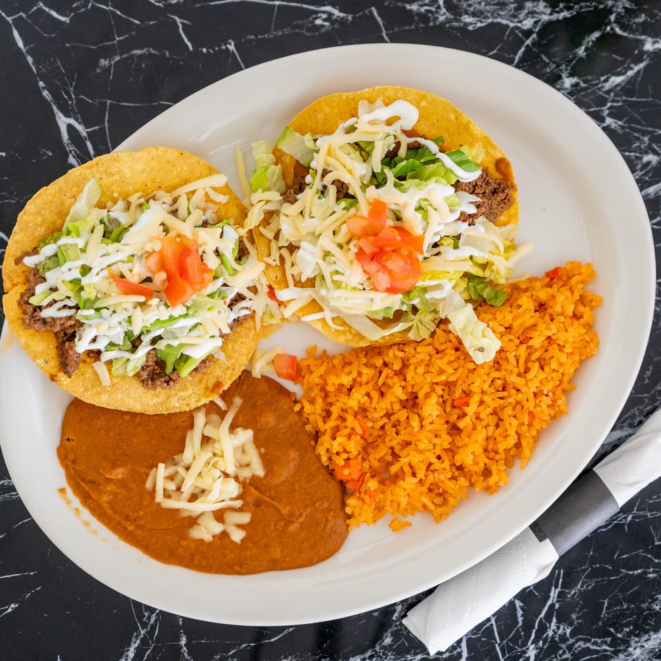 Two crispy tacos with ground beef, lettuce, cheese, and tomatoes, served with rice and refried beans.