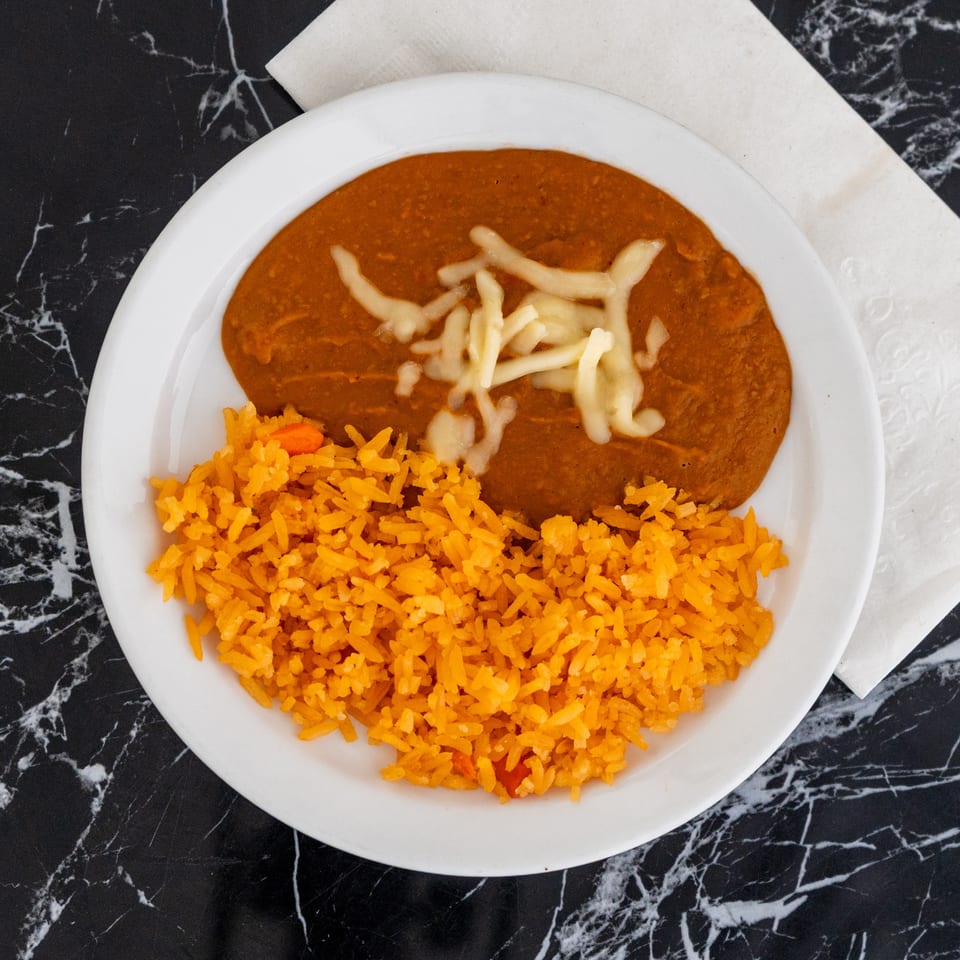 A white plate with refried beans topped with cheese and a side of orange rice.