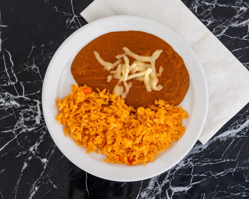 A white plate with refried beans topped with cheese and a side of orange rice.