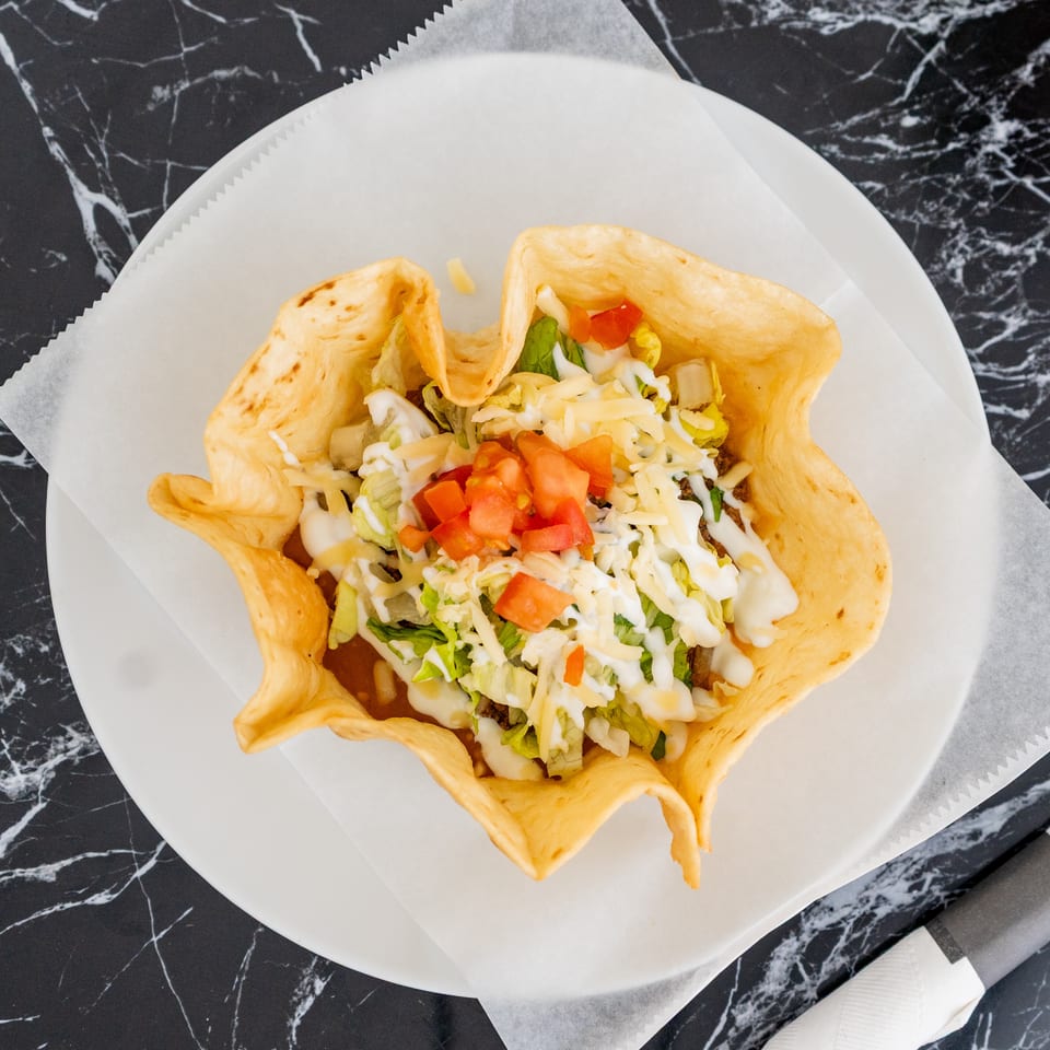 Taco salad in a crispy tortilla bowl, topped with lettuce, cheese, tomatoes, and sour cream.
