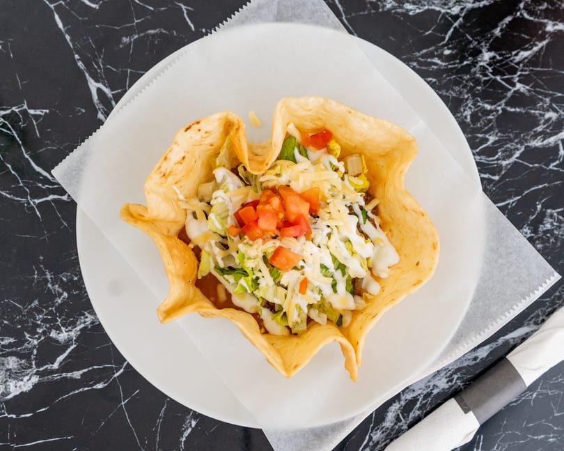 Taco salad in a crispy tortilla bowl, topped with lettuce, cheese, tomatoes, and sour cream.