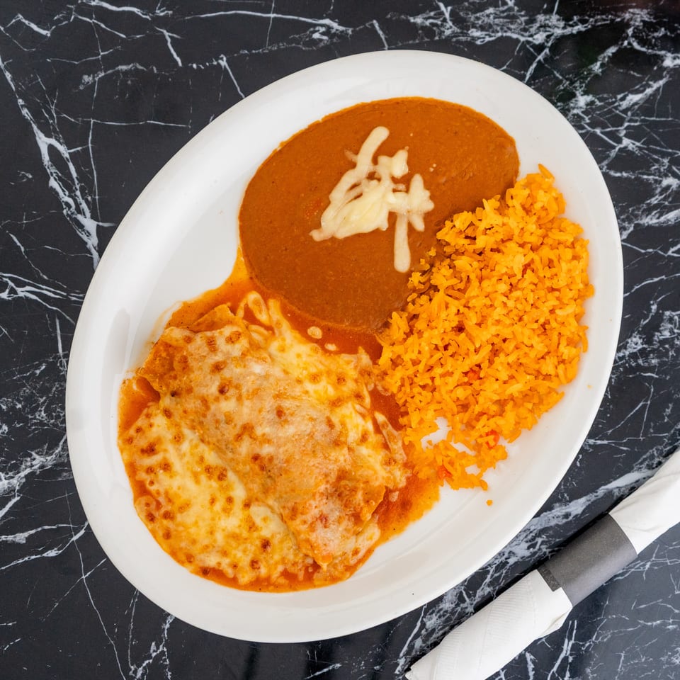 A plate of enchiladas covered in melted cheese, with a side of rice and refried beans.