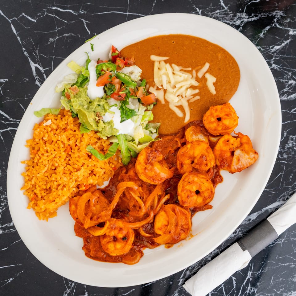 A white plate with shrimp in red sauce, rice, refried beans, and a side salad.