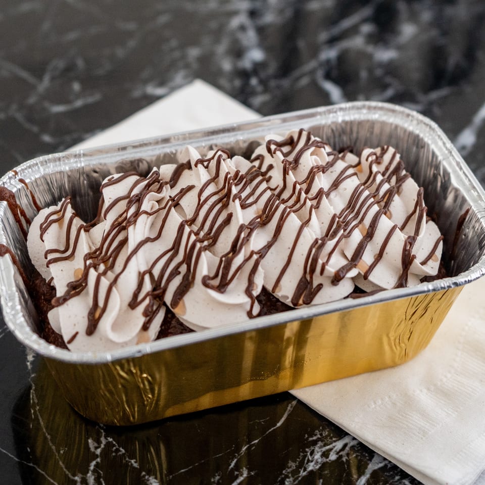 Chocolate cake with white whipped cream and chocolate drizzle in a gold and silver foil pan.