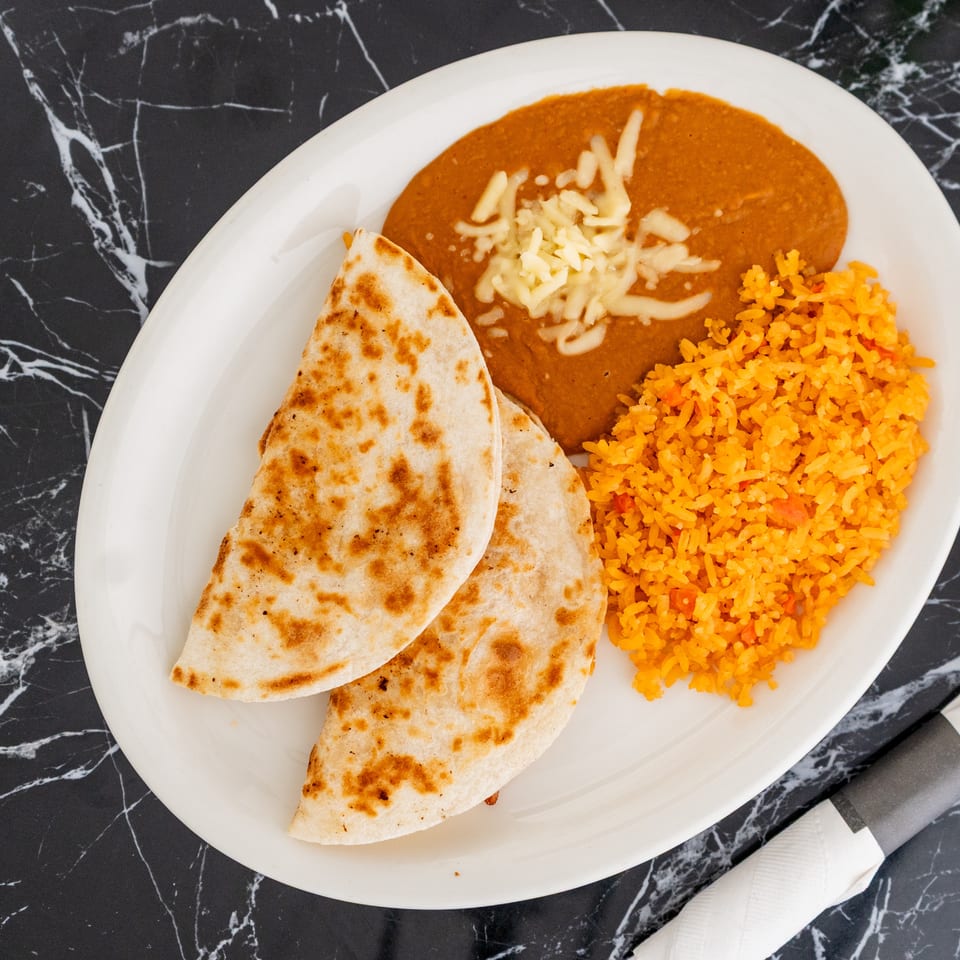 A white oval plate with two quesadillas, refried beans with cheese, and orange rice.